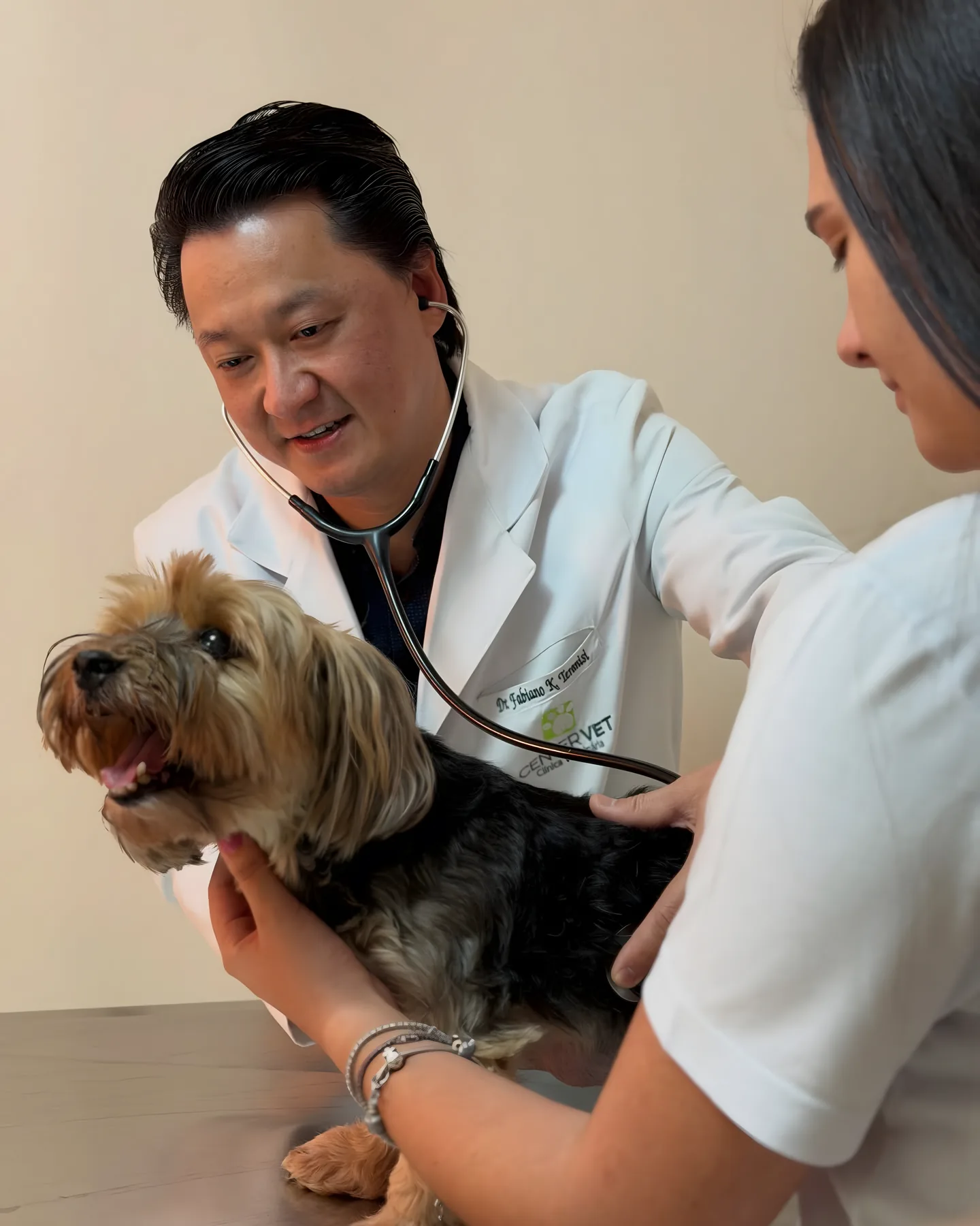 Dr. Fabiano auscultando um Yorkshire sobre a mesa, com a tutora ao lado